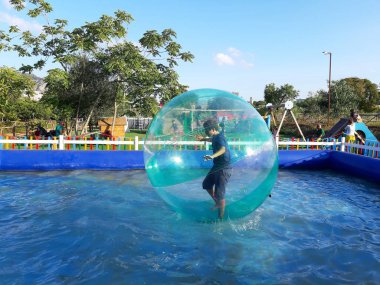 Havuzda yüzen şişme topun içinde eğlenen çocuk görüntüsü.
