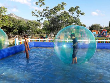 Havuzda yüzen şişme topun içinde eğlenen çocuk görüntüsü.