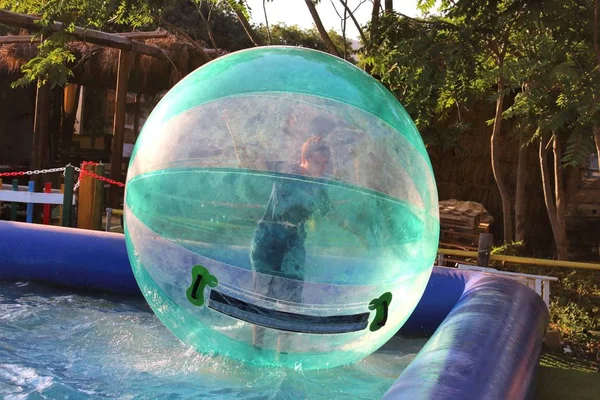 Havuzda yüzen şişme topun içinde eğlenen çocuk görüntüsü.