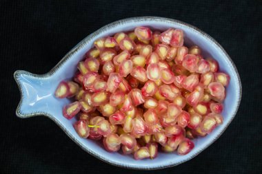 Sağlıklı parmak yiyecekleri için hazır olan nar tanelerinin canlandırıcı görüntüsü açık mavi bir kasede siyah arka planda servis ediliyor.