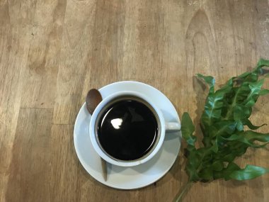 sıcak siyah Amerikalı kahve coaster ve tahta kaşık ve ahşap doğal kahverengi masa lambası kafede taze yeşil yaprağı ile beyaz Kupası