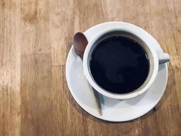 sıcak siyah Amerikalı kahve coaster ve ahşap doğal kahverengi masa lambası kafede üzerinde tahta kaşık ile beyaz seramik Kupası