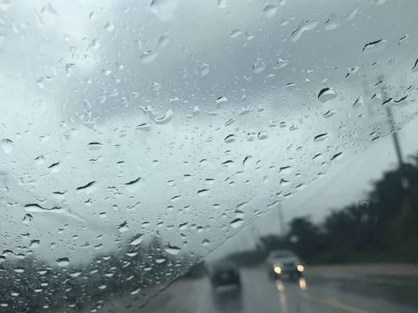 从汽车前挡风玻璃上看到乡村道路 在雨中行驶时 以雨滴为前景 前部有一辆汽车 另一辆汽车朝相反的方向驶来 — 图库照片