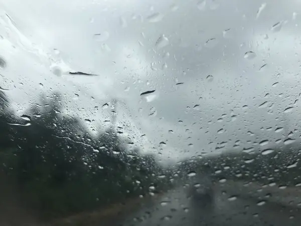 車からぼやけ道路シーンたっぷり雨滴のフロント ガラスをフロントし ほとんど雨が降っているときにフロントと嵐に一台の車を見る — ストック写真