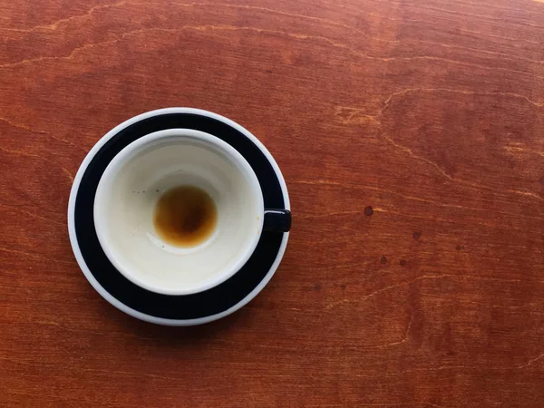 Cangkir keramik hitam dan piring kopi hitam panas yang sudah habis di atas meja kayu — Stok Foto