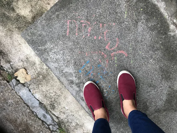 Kadınlar beton yolda duran kot pantolon ve kırmızı ayakkabılar giyer.