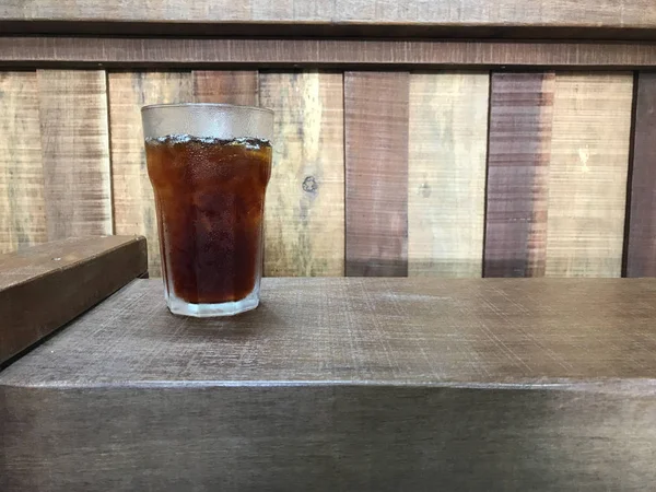 iced black coffee in glass without straw on natural color wood chair