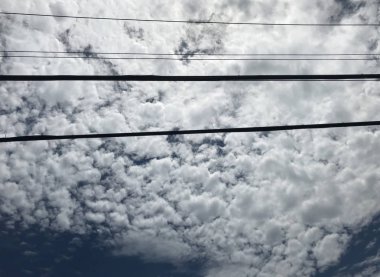 Pamuk bulutlar ve siyah elektrik ve kablo kablolarıyla koyu mavi gökyüzü.