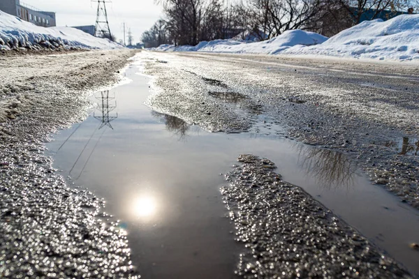 Droga z strumieniami wiosny, które płyną wzdłuż drogi pokrytej lodem i gęstym śniegiem, odbicie słońca, selektywne skupienie — Zdjęcie stockowe