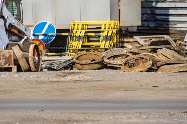 Bir yığın eski rögar kapağı iyi satılmış rögar kapakları yığılmış bir yığın, geçici yol işaretleri ve acil durum bariyerlerinin yanında.