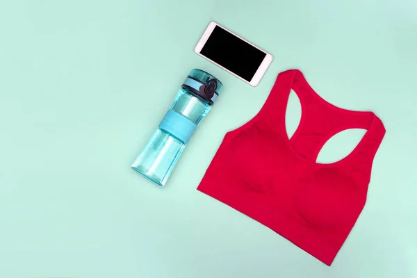 The concept of home workouts. Sports top, water bottle, phone on a turquoise background. Flat lay.