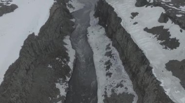 İHA, Dettifoss Şelalesi altında nehrin yukarısında uçar ve kamerayı yukarı eğerek tüm şelaleyi yavaşça ortaya çıkarır. Drone shot: etkileyici bulutlu havalarda Dettifoss Şelalesi