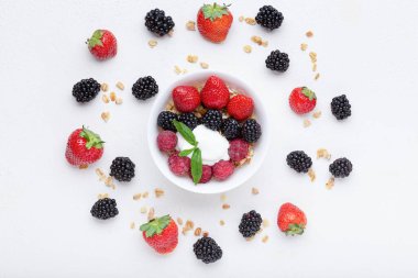 Beyaz arka planda çilekli, yaban mersinli, ahududu ve yoğurtlu meyve salatası kasesi. Düz, üst görünüm yaz sağlıklı konsept.