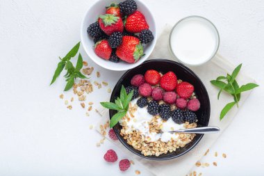 Yoğurt kasesi taze böğürtlen ve tahıl gevreği beyaz arka planda servis ediliyor, yukarıdan geliyor. Yaz sağlıklı kahvaltı konsepti.