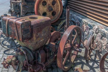 Geçen yüzyılın eski, paslı tarım makineleri, hangarın yanında duruyor..
