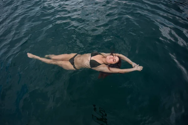 A jovem está deitada na água nas costas. Mulher bonita em um biquíni verde está deitada de costas na água . — Fotografia de Stock