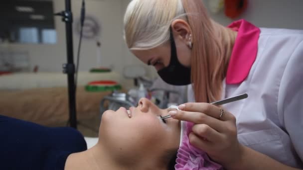 Professional beautician undergoing eyelash extension procedure. Master and a client in a modern beauty salon — Stock Video