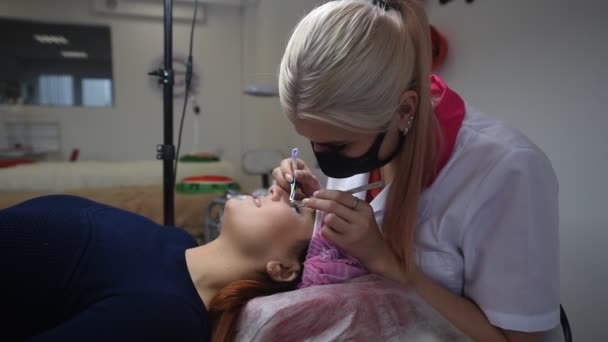 Professional beautician undergoing eyelash extension procedure. Master and a client in a modern beauty salon — Stock Video