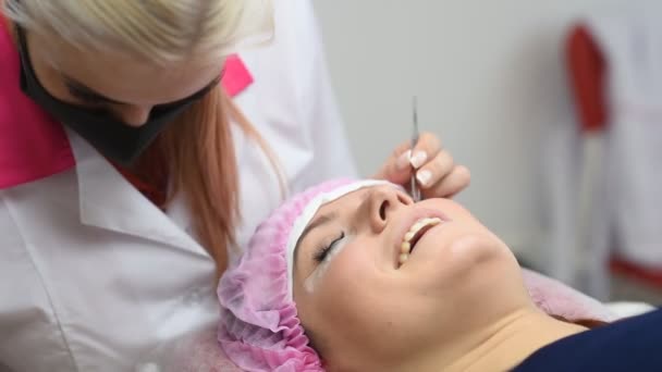 Профессиональный косметолог проходит процедуру наращивания ресниц. Мастер и клиент в современном салоне красоты — стоковое видео