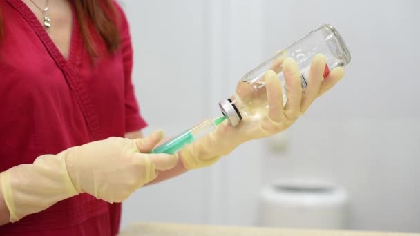 一名身穿红色医疗服的年轻护士从玻璃瓶中放入一次性注射器药物中。兽医. — 图库视频影像