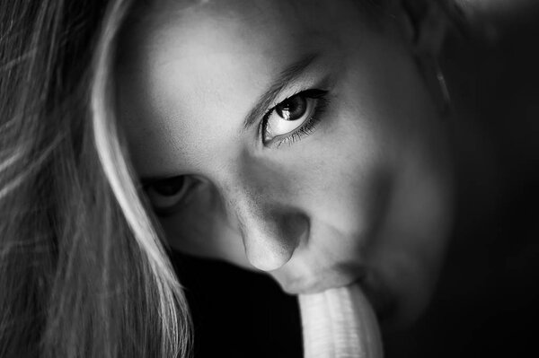 Молодая девушка эротически облизывает и сосёт банан и смотрит ей в глаза. Имитирует оральный секс
