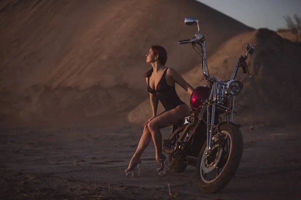 Femme aux cheveux rouges en lingerie sexy en talons hauts s'assoit sur une moto. Attrayant fille aux cheveux roux assis sur une moto au coucher du soleil — Photo