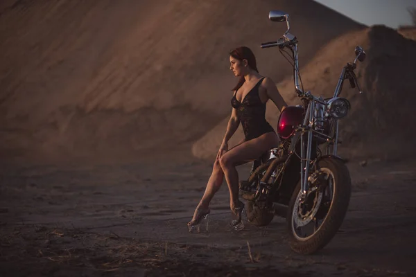 Mujer pelirroja en lencería sexy en tacones altos se sienta en una motocicleta. Atractiva chica pelirroja se sienta en una motocicleta al atardecer — Foto de Stock