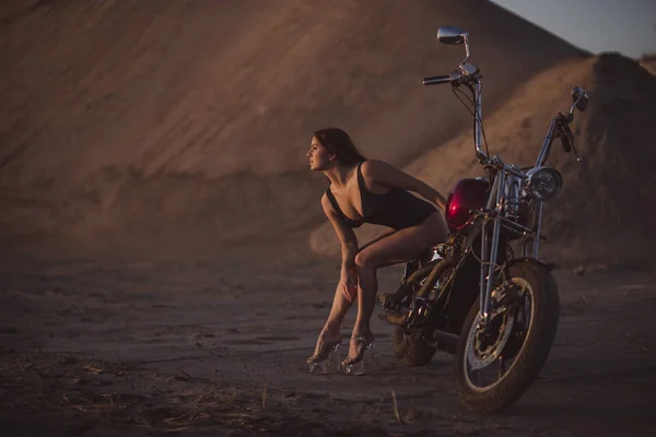 Femme aux cheveux rouges en lingerie sexy en talons hauts s'assoit sur une moto. Attrayant fille aux cheveux roux assis sur une moto au coucher du soleil — Photo