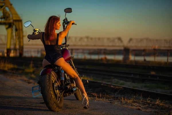 Rödhårig kvinna i sexiga underkläder i höga klackar sitter på en motorcykel. Attraktiv rödhårig flicka sitter på en motorcykel vid solnedgången — Stockfoto