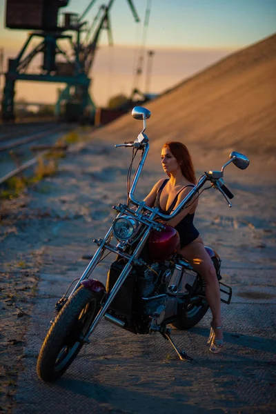 Femme aux cheveux rouges en lingerie sexy en talons hauts s'assoit sur une moto. Attrayant fille aux cheveux roux assis sur une moto au coucher du soleil — Photo