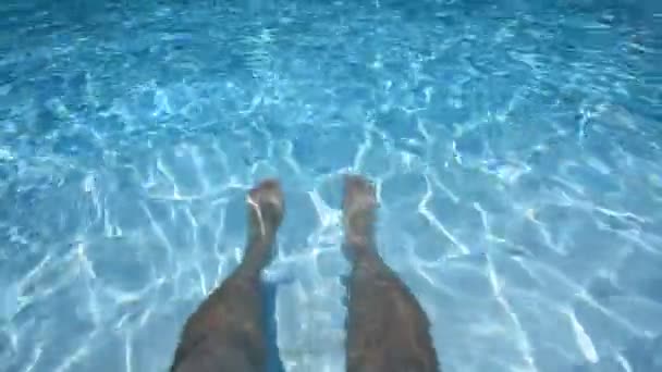 Волохаті чоловічі ноги в блакитній прозорій воді, відкритий басейн, сонячне світло . — стокове відео