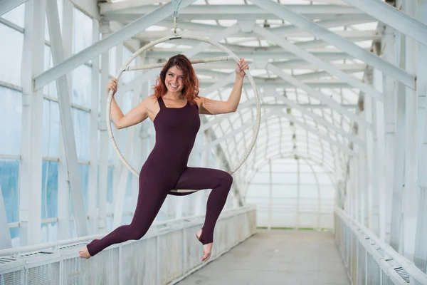 La gymnaste aérienne aux cheveux roux dans un combo sportif se produit au cerceau aérien dans un passage pour piétons . — Photo