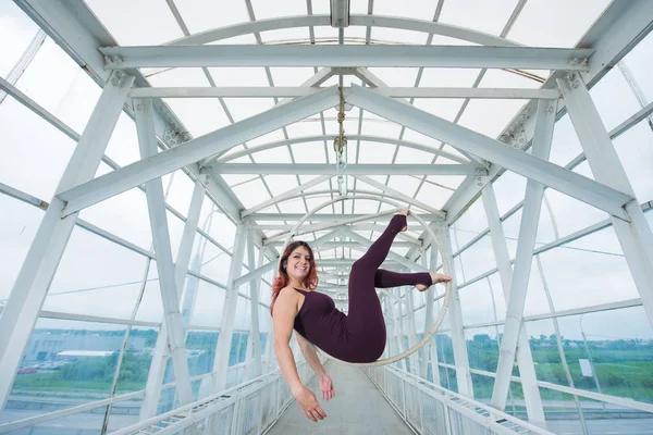 La gymnaste aérienne aux cheveux roux dans un combo sportif se produit au cerceau aérien dans un passage pour piétons . — Photo