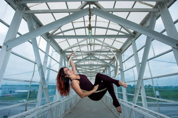 La gymnaste aérienne aux cheveux roux dans un combo sportif se produit au cerceau aérien dans un passage pour piétons . — Photo