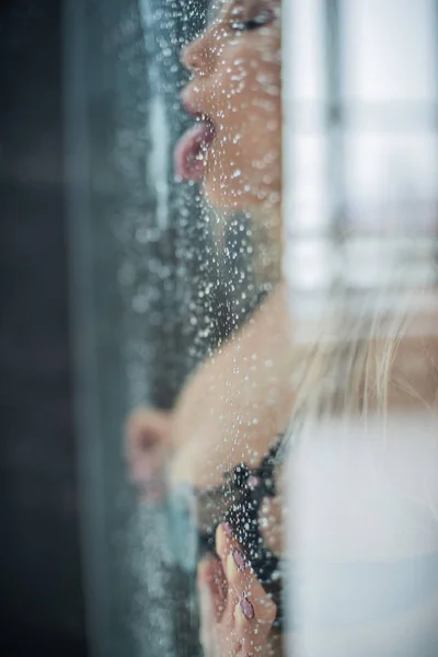 Chica europea en ropa interior negra, presionó su pecho y las manos para el vidrio húmedo y la lengua lamiendo eróticas gotas. — Foto de Stock