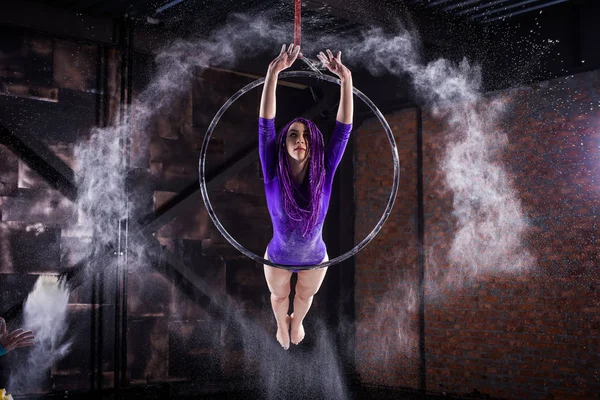 Una ragazza giovane e snella con un body alla lavanda e dei terrori lilla, che fa ginnastica sull'anello dell'aria, il cerchio e getta le mani della polvere bianca sotto forma di nuvola . — Foto Stock