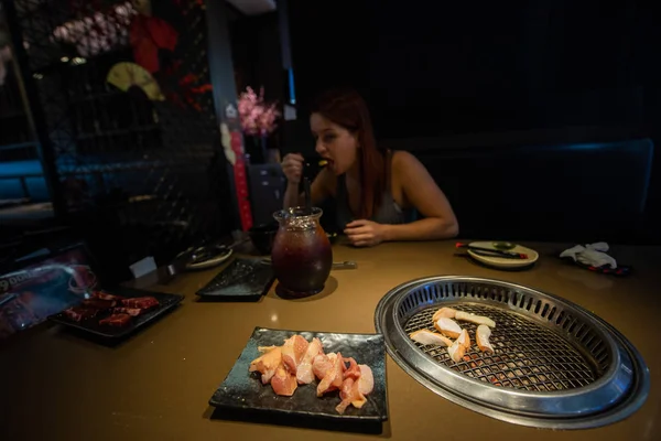 Una donna dai capelli rossi mangia in un caffè coreano. Grigliare carne in un ristorante coreano. Cibo tradizionale coreano . — Foto Stock