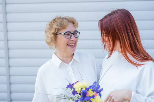 Dospělá dcera dává květiny své matce venku na dvorku domu. Trávit čas spolu, oslavovat doma o víkendech. Den matek. Teplé mezigenerační vztahy — Stock fotografie