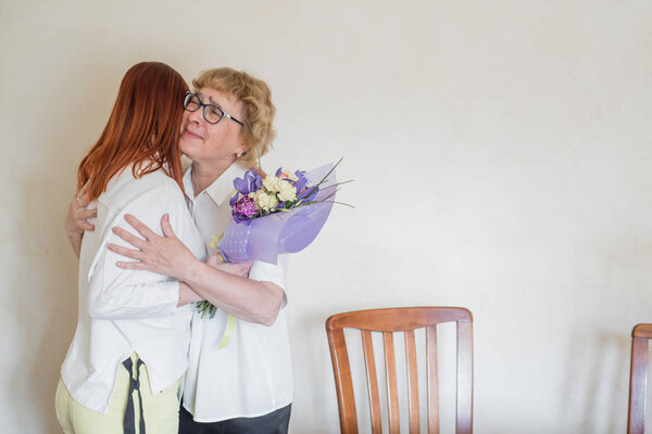 Дочь дарит цветы взрослой матери. Дочь дарит цветы своей матери и обнимает её. Проводим время вместе, празднуем дома по выходным. День матери
