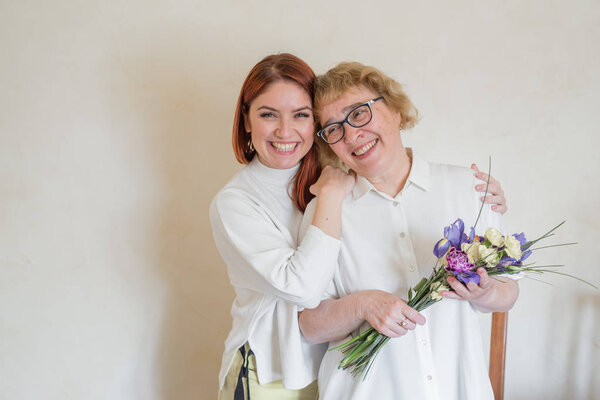 Дочь дарит цветы взрослой матери. Дочь дарит цветы своей матери и обнимает её. Проводим время вместе, празднуем дома по выходным. День матери
