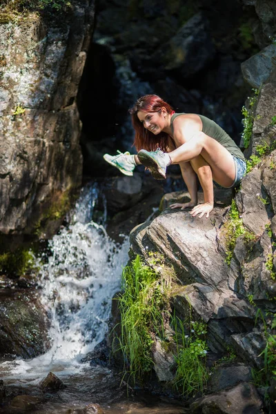 Red-haired woman in shorts doing yoga at the waterfall. The girl is standing in the pose of a firefly, titibhasana — Stock Photo, Image