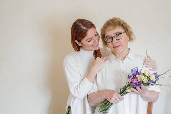 Дочь дарит цветы взрослой матери. Дочь дарит цветы своей матери и обнимает её. Проводим время вместе, празднуем дома по выходным. День матери
