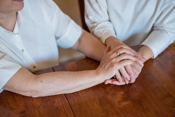 Elderly mother and her daughter holding hands while sitting at the table.Close up on women of different generations holding hands. Close Up Shot Of Mother And Daughter's Hands Holding — Stock Photo, Image