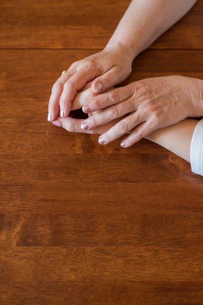 Elderly mother and her daughter holding hands while sitting at the table.Close up on women of different generations holding hands. Close Up Shot Of Mother And Daughter's Hands Holding — Stock Photo, Image