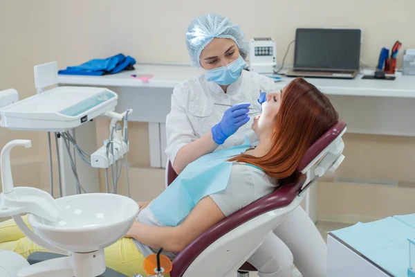 Mujer dentista revisando a su paciente en busca de caries. Mujer pelirroja examinada por un médico. La chica hará la salud de los dientes . —  Fotos de Stock