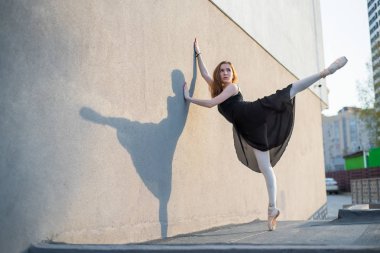 Balerin tutu duvara yakın ayakta poz. Siyah elbiseli ve dışarıda dans eden güzel genç bir kadın. Muhteşem balerin açık havada dans yapıyor