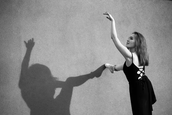 Ballerina in Tutu poseren staande in de buurt van de muur. Mooie jonge vrouw in zwarte jurk en Pointe dansen over stad achtergrond. Prachtige ballerina die een dans buitenshuis uitvoert. Zwart-wit — Stockfoto