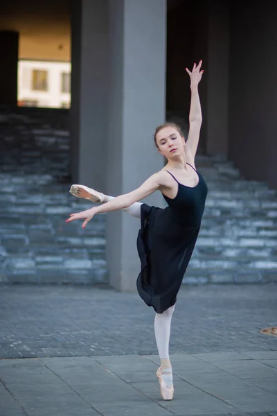 Ballerine dans un tutu posant sur fond d'immeuble résidentiel. Belle jeune femme en robe noire et pointes chaussures de danse ballet extérieur . — Photo