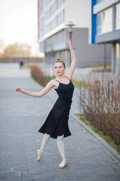 Ballerine dans un tutu posant sur fond d'immeuble résidentiel. Belle jeune femme en robe noire et pointes chaussures de danse ballet extérieur . — Photo