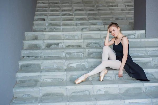 Ballerine en tutu posant assise sur les escaliers Une belle jeune femme en robe noire et chaussures pointes se repose assise dans une pose élégante sur les escaliers de l'extérieur — Photo